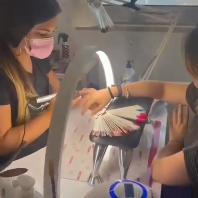 Manicure a aplicar verniz numa cliente com amostra de vernizes em leque sobre a mesa