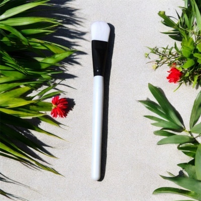 Pincel de maquilhagem sobre superfície clara com folhas verdes e flores vermelhas