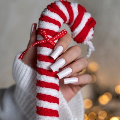 Mão com unhas brancas segurando bastão de doces felpudo vermelho e branco com laço