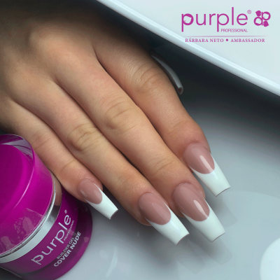 Mão com unhas artificiais de ponta branca junto a pote roxo de produto para unhas