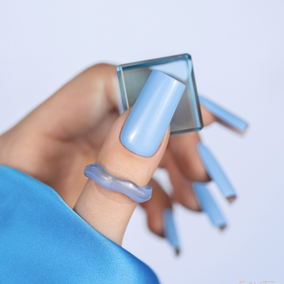 Mão com unhas azuis a segurar embalagem de verniz com anel translúcido azul