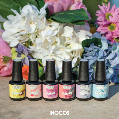 Seis vernizes de unhas INOCOS de várias cores com flores artificiais ao fundo