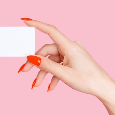 Mão feminina com unhas pintadas de laranja segurando um cartão branco