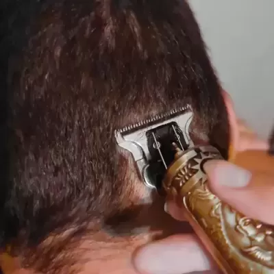 Máquina de cortar cabelo dourada a aparar cabelo castanho num fundo cinza