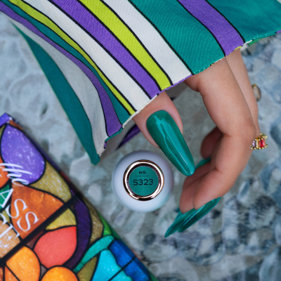 Mão com unhas verdes longas segurando frasco de verniz S323 com manga colorida às riscas.