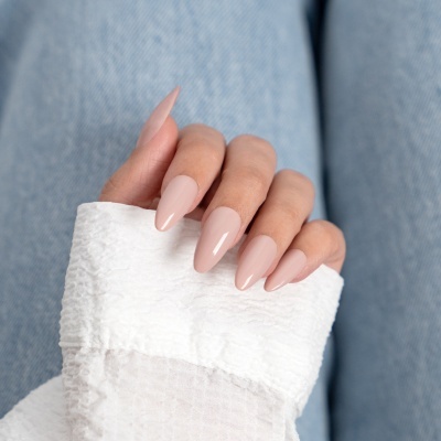 Unhas postiças nude brilhantes em mão segurando manga branca, fundo jeans azul