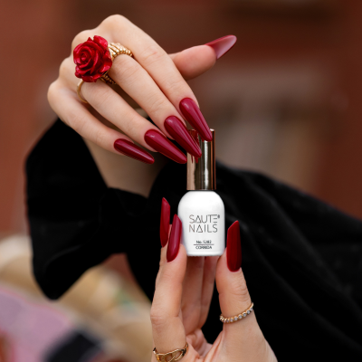 Frasco de verniz SAUTE NAILS número 5282 CORRENTE segurado por mãos com unhas vermelhas e anéis