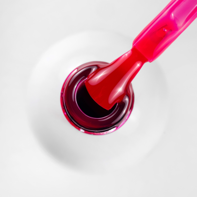 Pincel rosa com verniz vermelho escuro num frasco branco de verniz de unhas