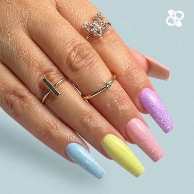 Mão com unhas compridas coloridas em tons pastel e anéis dourados.