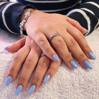 Mãos femininas com unhas azul claro, anel e pulseira prateados sobre toalha branca.