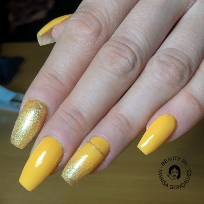Unhas pintadas com verniz amarelo e dourado brilhante em fundo de madeira
