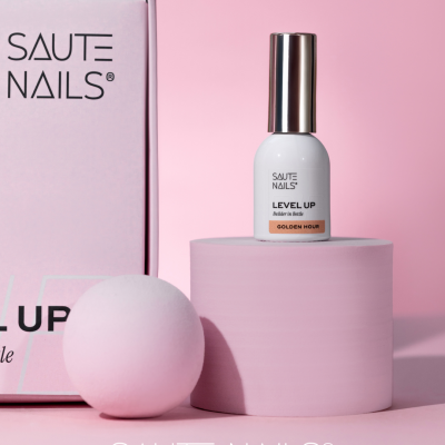 Frasco branco de verniz de unhas SAUTE NAILS sobre cilindro rosa com esfera e caixa rosa ao fundo