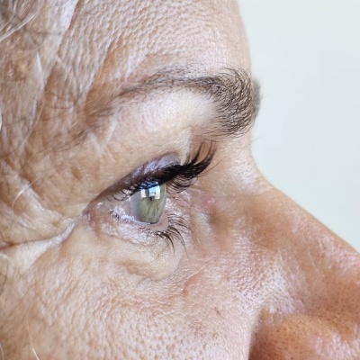 Close-up do lado direito do rosto de uma pessoa idosa com pele enrugada e olho verde