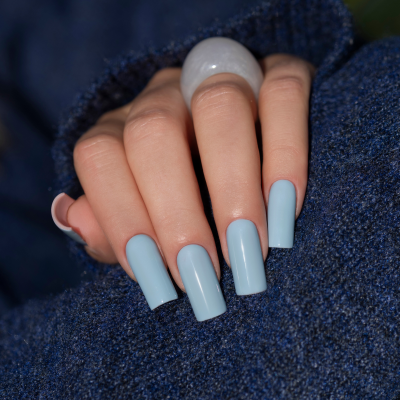 Unhas compridas azuis claras brilhantes em mão feminina com anel transparente e roupa azul escura