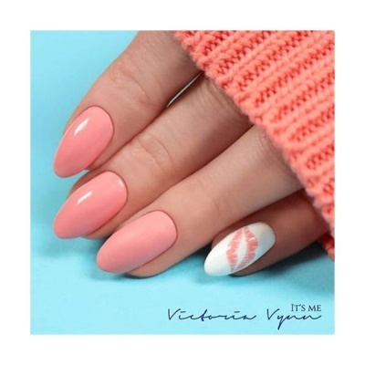 Unhas decoradas em rosa e branca com desenho de lábios numa mão sobre fundo azul e malha cor-de-rosa.