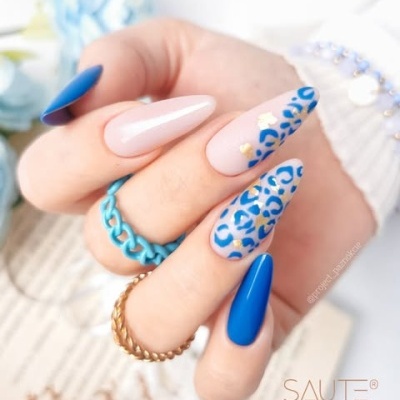 Unhas com gel azul e bege com padrão de oncinha azul e anéis azuis e dourados