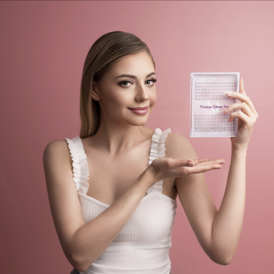 Mulher loira segurando um folheto transparente com texto 'Premium Volume Tray' num fundo rosa