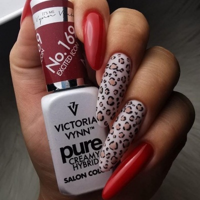 Frasco de verniz de unhas Victoria Vynn segurado por mão com unhas vermelhas e unhas com padrão de leopardo