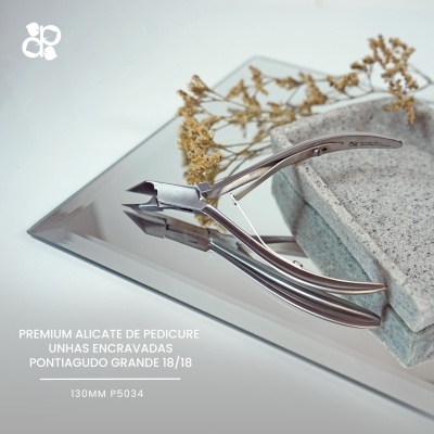 Alicate de pedicure metálico prateado em superfície espelhada com base de pedra cinzenta e ramos secos