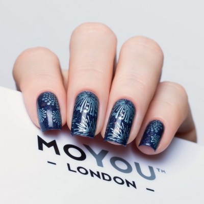Unhas com verniz azul escuro com padrão prateado segurando embalagem MOYOU LONDON