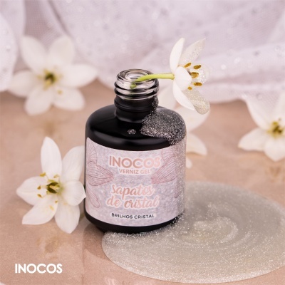 Frasco preto de verniz gel com rótulo branco e rosa da marca INOCOS e flores brancas ao redor