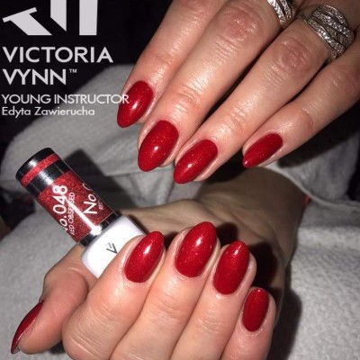 Mãos com unhas vermelhas brilhantes segurando garrafa de verniz Victoria Vynn