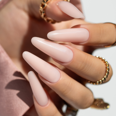 mão feminina com unhas nude foscas e anéis dourados em fundo branco e rosa