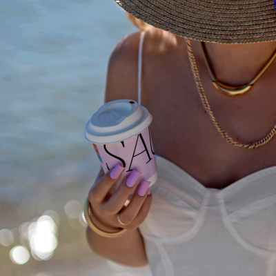 Pessoa de chapéu de palha segurando chávena de café na praia