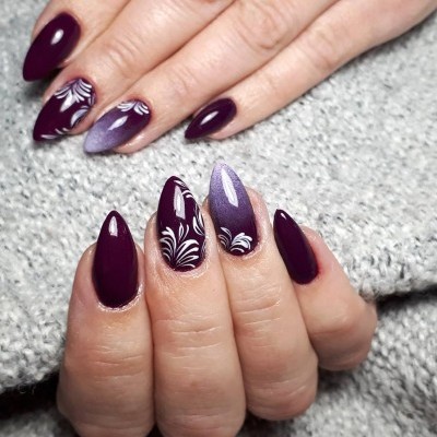 Unhas roxas com decoração floral branca em fundo cinzento.