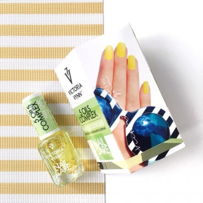 Frasco de verniz amarelo da Victoria Vynn ao lado da sua caixa com imagem de mão e óculos de sol