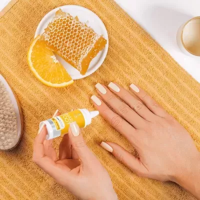 Óleo de cutícula com favo de mel, laranja e mãos femininas em toalha amarela