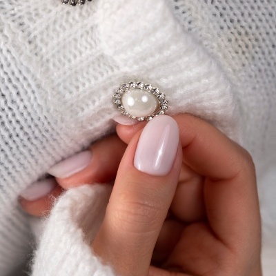 Unhas rosa claro segurando malha branca com botões decorativos prateados