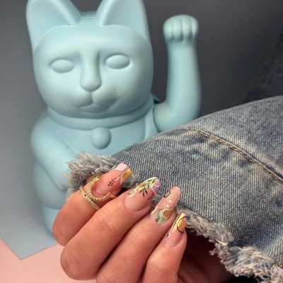 Mão com unhas decoradas e anéis ao lado de figura decorativa de gato azul
