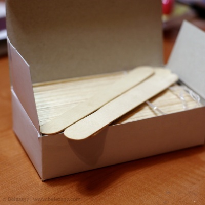 Espátulas de madeira clara dentro de caixa branca sobre mesa de madeira.