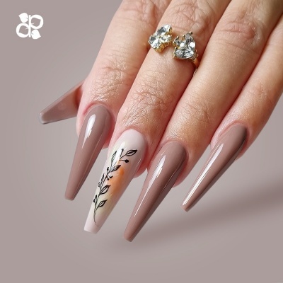 Mão com unhas postiças longas, nude e desenho floral, com anel dourado e pedras