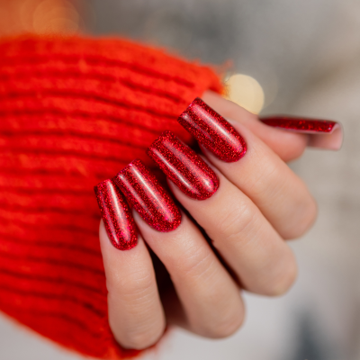 Unhas compridas com verniz vermelho brilhante e brilhos, mão com manga vermelha