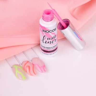 Verniz rosa INOCOS aberto com pincel e unhas decoradas coloridas em fundo branco e tecido rosa