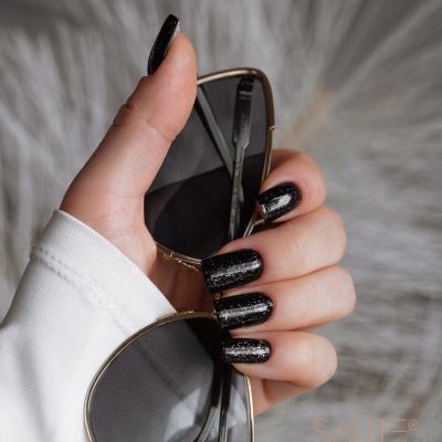 Mão com unhas pretas brilhantes segurando óculos de sol dourados com lentes escuras