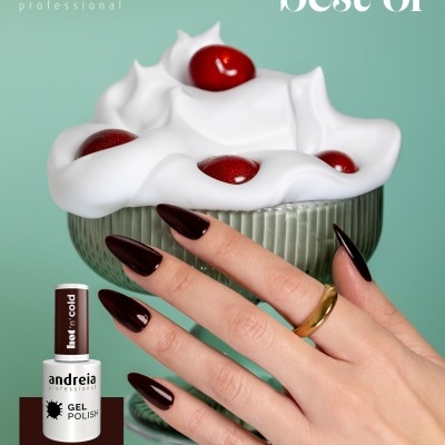 Mão com unhas castanhas escuras e copo com cobertura branca e frutos vermelhos