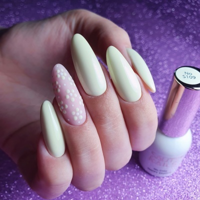 Unhas compridas amarelas com bolinhas brancas e verniz gel, frasco de verniz no fundo roxo