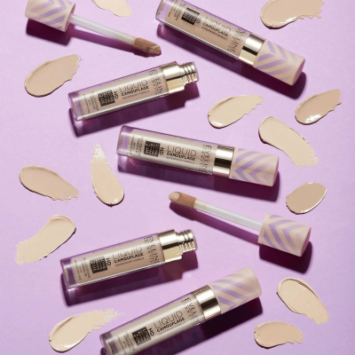 Corretor líquido em tubos lilás com padrão de setas cinzas e manchas do produto sobre fundo lilás