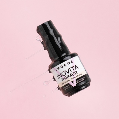 Frasco preto de primer para unhas com etiqueta branca e gotas de líquido transparente em fundo rosa