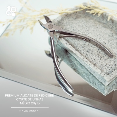 Alicate de pedicure metálico prateado sobre pedras claras e superfície espelhada