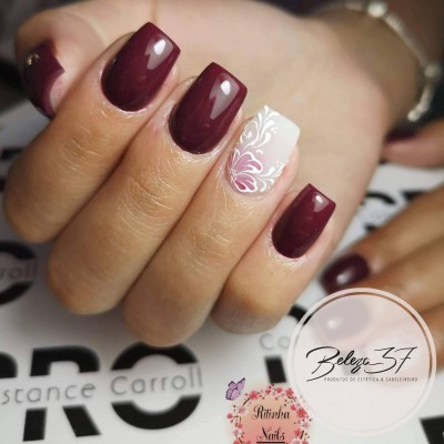 Unhas postiças vinho escuro e branca com padrão floral rosa num fundo com texto e logótipos.