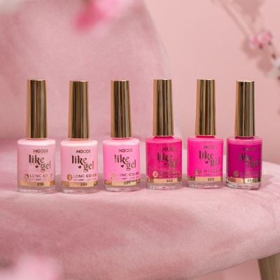 Seis frascos de verniz gel rosa da marca INOCOS com tampas douradas sobre tecido rosa com fundo floral desfocado