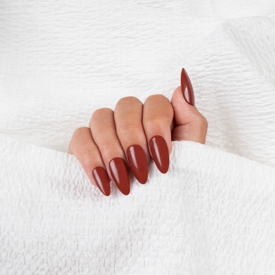 Mão com unhas castanho avermelhado sobre tecido branco texturizado