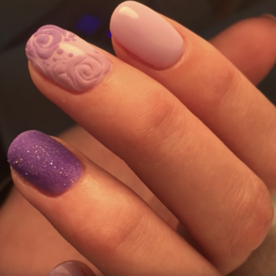 Mãos femininas com unhas esmaltadas lilás e rosa claro com decoração 3D de rosas e glitter