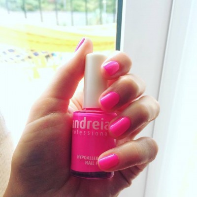 Frasco de verniz de unhas rosa fluorescente com tampa branca segurado por mão com unhas pintadas de rosa