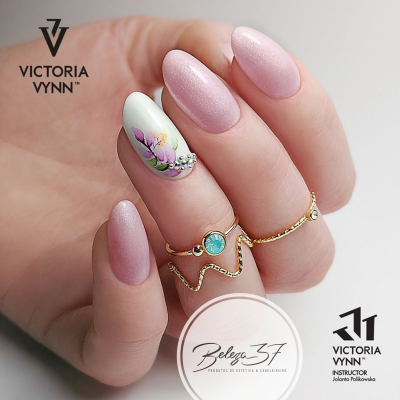 Unhas decoradas com verniz rosa perolado e unha branca com desenho floral e strass, com anéis dourados.