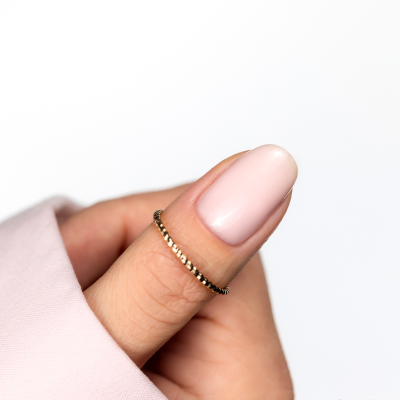 Anel dourado texturizado em dedo com unhas rosa claro